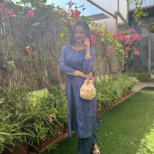 Woman posing outdoors in a dusty slate blue Chanderi dyeable Chikankari style embroidered kurti with matching palazzo pants set holding a potli bag